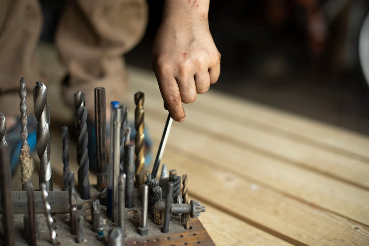 Man takes drill bit. Details of craft. Tools in garage. Worker chooses nozzle for drill.