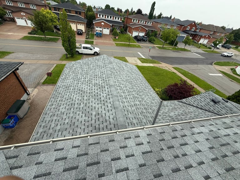 Aerial view of a residential driveway with gray patterned pavers, green lawn, and suburban homes in the background