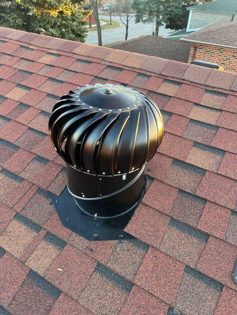 Black metal roof turbine vent mounted on red shingle roof of residential home
