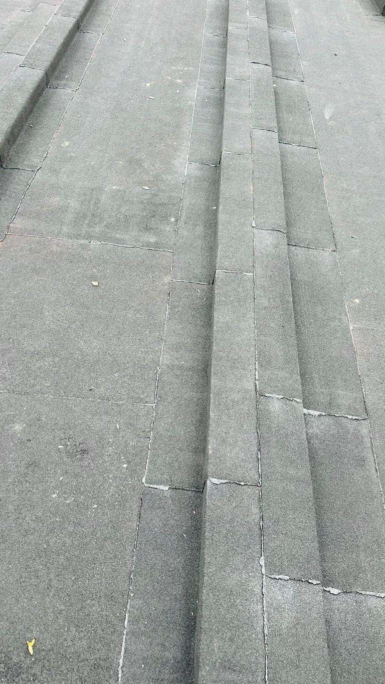 Gray concrete pavement with rectangular tiles laid in a diagonal brick pattern, showing worn surfaces and mortar lines