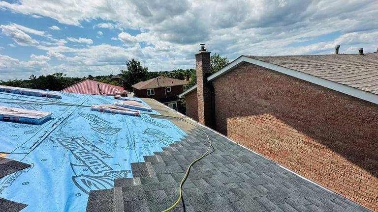 Roofing construction in progress on a brick house with blue protective covering and new shingles being installed